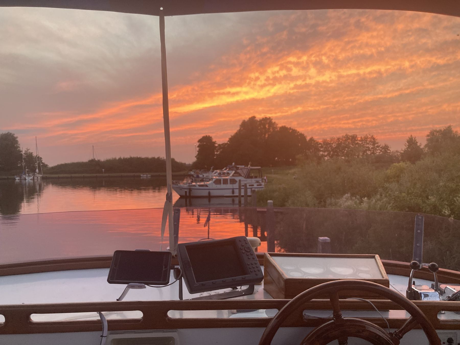 Steuerstand eines Trawlers am Abend: Tablet und Plotter auf Teak, dahinter Sonnenuntergang über dem Wasser